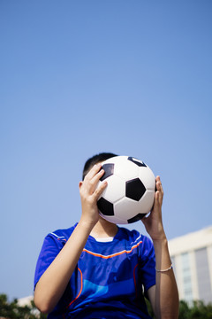在蓝天下，一个男孩把足球举到脸前。