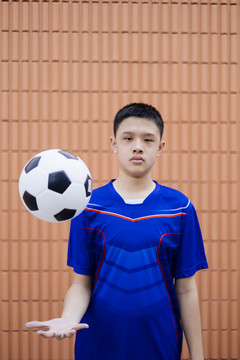 一个男孩站在棕色的墙前，把球抛向空中。