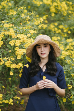 一个卷曲的长发女孩站在树上的黄花旁，手里拿着花的肖像照。