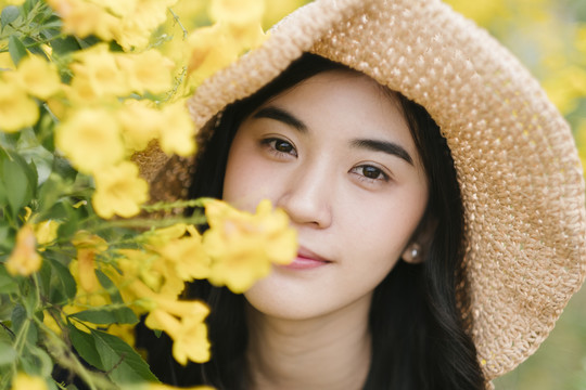 特写镜头中的泰国女孩站在黄色的花丛中看着那朵花。