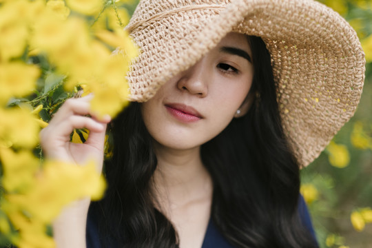 黄色花丛中戴棕色帽子的漂亮女孩的特写镜头。