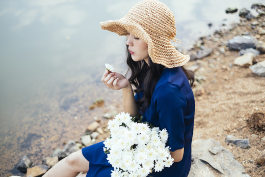 卷曲的长发女孩坐在湖边的岩石上欣赏手中的白花。