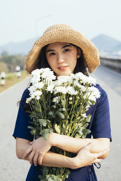 身着深蓝色连衣裙的可爱女孩抱着坝上的白花的中写真。