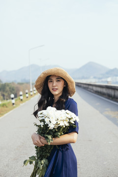 一个美丽的泰国女孩抱着白色的花朵站在水坝的路上。