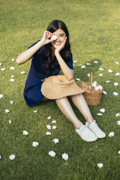 一头卷曲长发的深蓝色女孩坐在田野里，微笑着把那朵白花举向阳光。