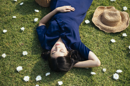 一个穿着深蓝色连衣裙的泰国女孩躺在草地上，周围开着白色的花。