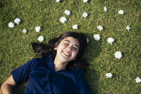 一个穿着深蓝色衣服的女孩躺在白花丛中的田野上，笑容满面。