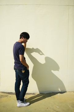 黑发人站在阳光下的墙上，他的影子。