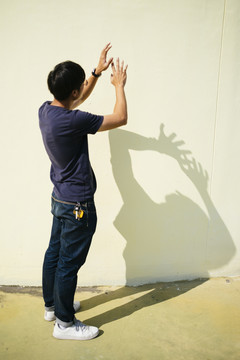 黑发男人站在阳光下的墙上，带着他的影子，假装要打篮球。