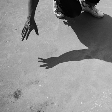 黑白裁剪的照片，一个男人坐在地板上，在阳光下，他的影子。