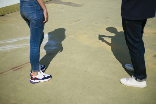 一对夫妇站在绿色的地板上享受他们的影子时，他们的腿的剪短图像。