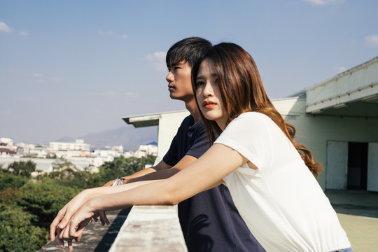 一对泰国夫妇站在蓝天下的屋顶上欣赏城市景色。