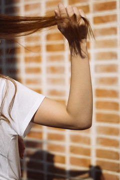女人的手在砖墙前拉着她深色头发的剪影。