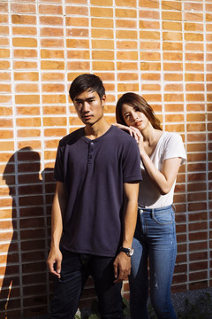 阳光下，一对泰国夫妇站在砖墙前。