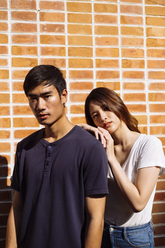 一对泰国夫妇站在砖墙前，一个女孩依偎着一个男人。