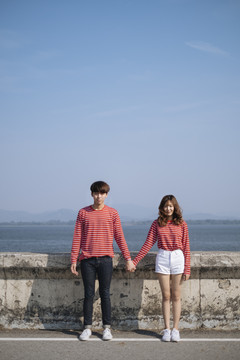 一对穿着红色t恤的年轻夫妇站在大坝的路上，手拉着手。