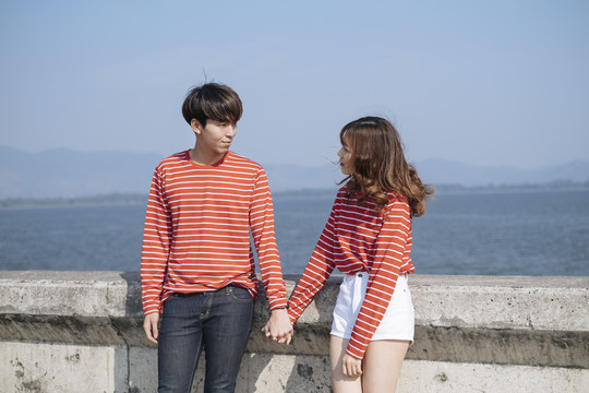 一对穿着红色t恤的年轻夫妇站在水坝边，手拉着手。