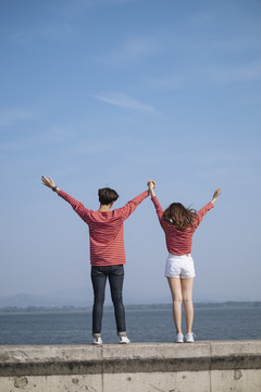 一对年轻的夫妇站在大坝的路障上，手举向天空，手拉着手。