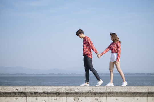 这对年轻夫妇走在大坝的路障上，手牵着手欣赏海景。