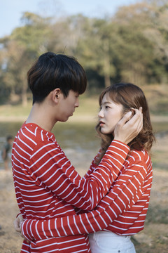 一对穿着红衣t恤的年轻夫妇在湖边互相拥抱，一个男孩抚摸着一个女孩的头发。