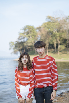 一对穿着红色t恤的夫妇站在森林的湖边。