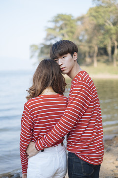一个穿着红衣t恤的男人抱着他女朋友的腰，他们站在湖边。