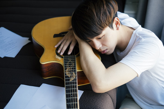 年轻的泰国吉他手躺在卧室里的原声吉他上感到沮丧。