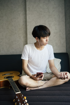 年轻的泰国吉他手在房间里用耳机听音乐练习吉他。