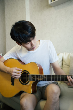 特写镜头：穿着白衬衫的泰国吉他手在客厅的沙发上弹原声吉他。
