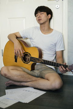 一个年轻的泰国吉他手厌倦了弹吉他，他靠在房间的门上睡觉。