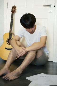 疲倦的年轻泰国吉他手男子睡在门口的房间在房子里。
