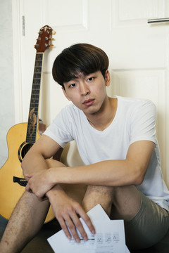 特写照片，年轻的泰国吉他手拿着抒情纸条坐在前门客厅里。