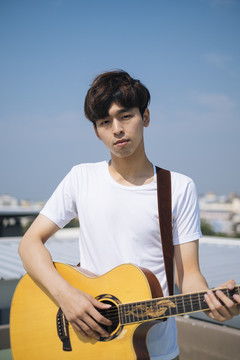 年轻的泰国吉他手的肖像男子与原声吉他户外屋顶。
