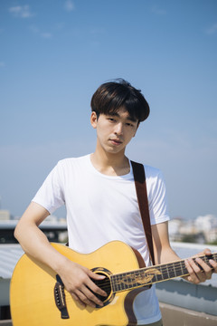 年轻的泰国吉他手的肖像男子与原声吉他户外屋顶。
