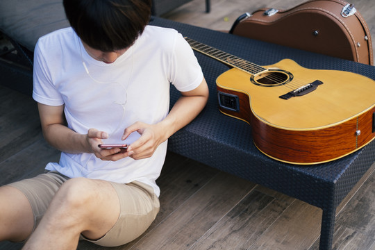 年轻的泰国吉他手在弹吉他之前先从智能手机上听音乐，寻找灵感。