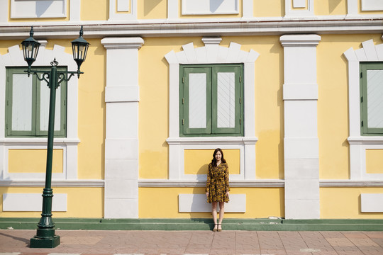 可爱的卷发黄裙女孩站在粉彩楼的人行道上。