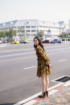 可爱的卷发女孩，穿着黄色连衣裙，站在路边的人行道上。