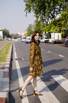 可爱的卷曲的长发女孩穿着黄色的裙子走过马路与斑马线。