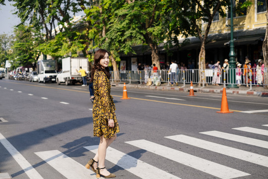 可爱的卷曲长发黄裙女孩与斑马线横穿马路，对着镜头微笑。
