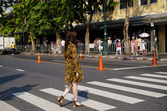 可爱的卷发黄裙女孩穿过斑马线，很多树和人在马路的另一边。