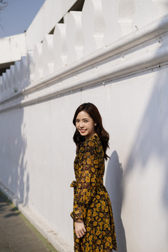 可爱的卷发女孩穿着黄色连衣裙站在阳光下的白色墙壁。