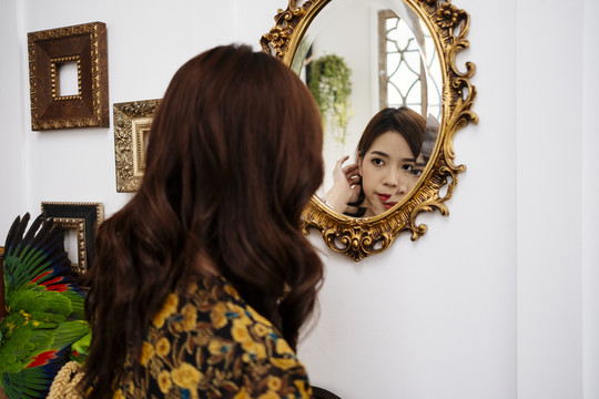 可爱的卷曲长发穿黄色连衣裙的女孩看着金色镜子里的自己。