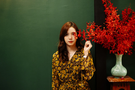 可爱的卷曲长发黄裙女孩站在绿墙前抢夺红花。