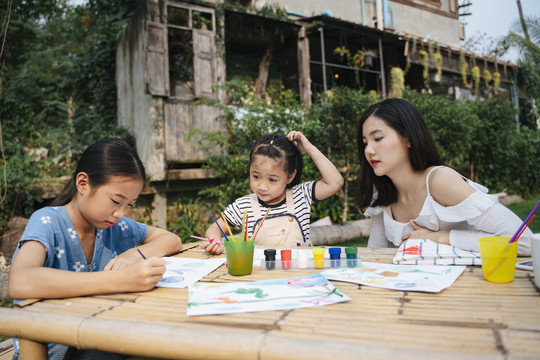 三姐妹在公园里喜欢在户外的纸上画水彩。孩子坐在桌子旁在纸上画画。年轻艺术家在纸上绘画。
