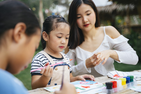 亚洲大姐帮小妹在户外的纸上画水彩。