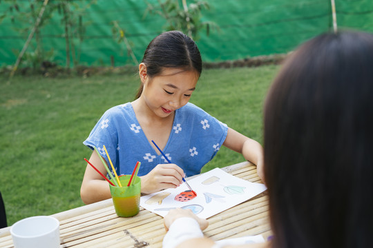 快乐的亚洲小女孩穿着蓝色衬衫在纸上画水彩。