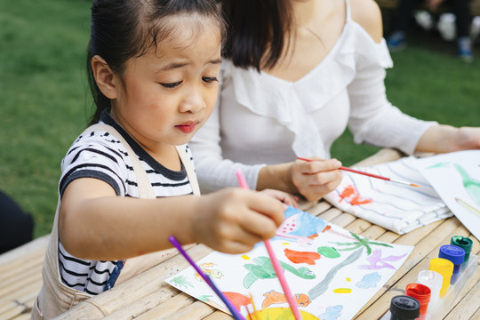 特写亚洲小女孩在户外用画笔在纸上画水彩。