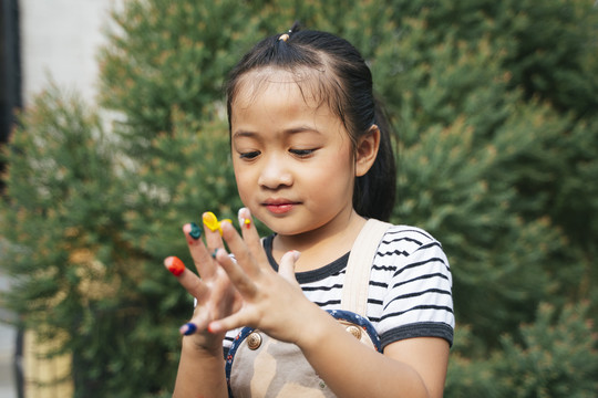 漂亮的女孩在玩手指上的颜色。一个亚洲女孩，手上涂着五颜六色的颜料，准备在花园里手绘。