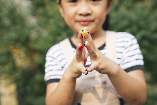在户外，一个可爱的亚洲小女孩正在用手指玩彩色游戏。