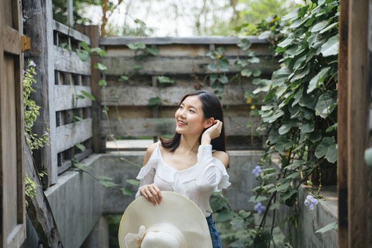 泰国亚裔年轻女子穿着性感的白色连衣裙，手持帽子在乡村花园。